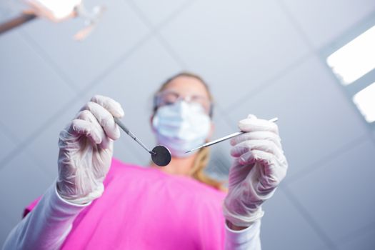 Dentist in surgical mask holding tools over patient at the dental clinic