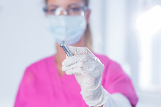 Dentist in surgical mask and scrubs holding tool at the dental clinic