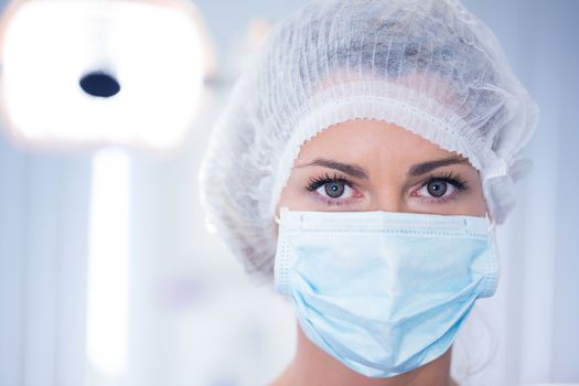 Dentist in surgical mask and cap looking at camera at the dental clinic
