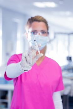 Dentist in surgical mask and scrubs holding syring at the dental clinic