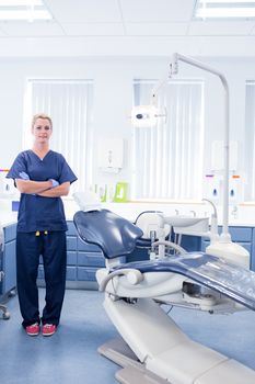 Dentist in blue scrubs standing with arms crossed at the dental clinic