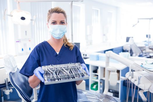 Dentist in blue scrubs holding tray of tools at the dental clinic