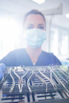 Dentist in blue scrubs showing tray of tools at the dental clinic