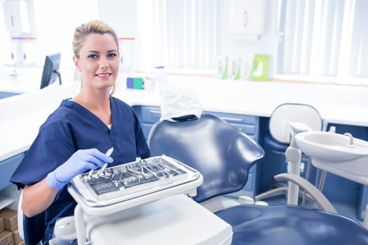 Dentist sitting with tray of tools smiling at camera at the dental clinic