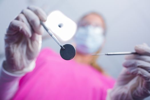 Dentist in surgical mask holding tools over patient at the dental clinic