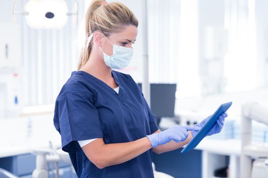 Dentist in mask and blue scrubs using her tablet at the dental clinic