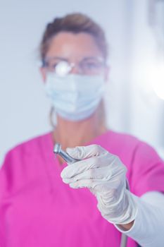 Dentist in surgical mask and scrubs holding tool at the dental clinic