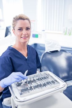 Dentist sitting with tray of tools smiling at camera at the dental clinic