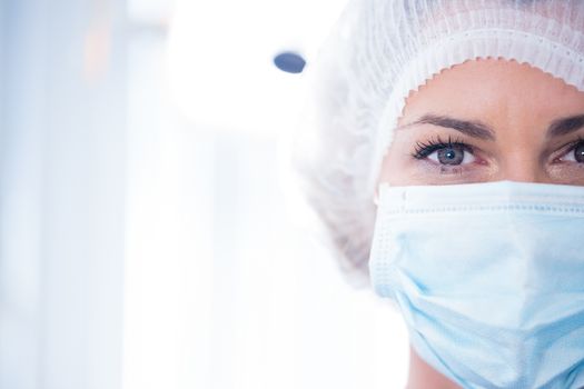 Dentist in surgical mask and cap looking at camera at the dental clinic