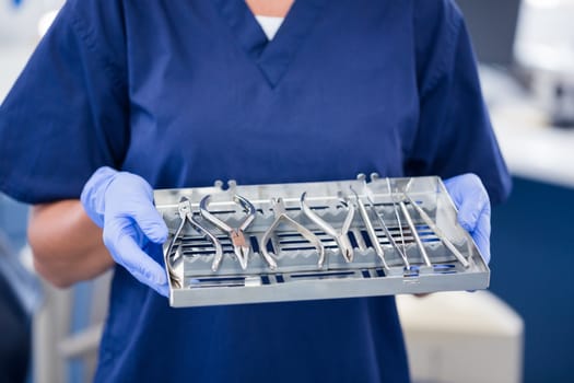 Dentist in blue scrubs holding tray of tools at the dental clinic