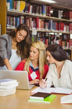 Pretty student showing her classmates something on laptop in library