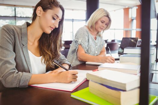 Matures females students writing notes at desk in library