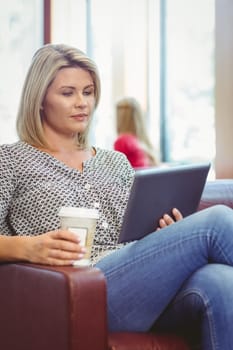 Woman using digital tablet and holding disposable cup in library