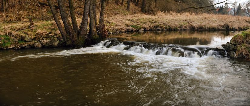 Panorama of a small weir on the river in early spring