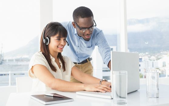 Smiling coworkers using laptop and headset in the office