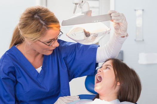 Pediatric dentist examining with a light her young patient in dental clinic