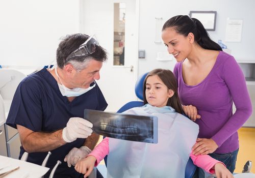 Pediatric dentist explaining to young patient and her mother the x-ray in dental clinic