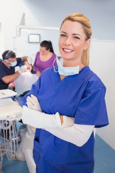 Nurse with folded arms with patient and dentist behind her in dental clinic