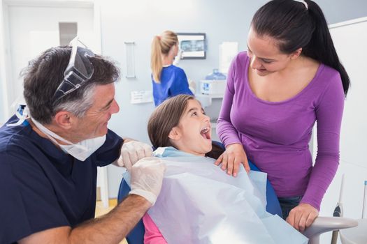 Smiling pediatric dentist with a happy young patient and her mother in dental clinic