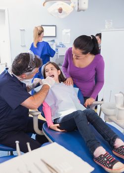 Pediatric dentist examining young patient with her mother in dental clinic