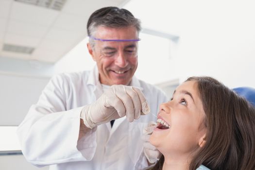 Pediatric dentist using dental floss to his young patient in dental clinic