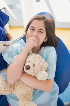 Scared patient covering mouth and holding teddy bear in dental clinic