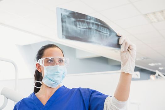 Dentist wearing surgical mask and safety glasses studying the x-ray