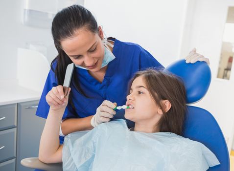 Pediatric dentist brushing teeth to her young patient in dental clinic