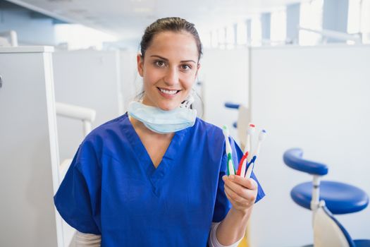 Portrait of a smiling dentist showing toothbrush in dental clinic