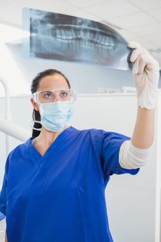 Dentist wearing surgical mask and safety glasses studying the x-ray