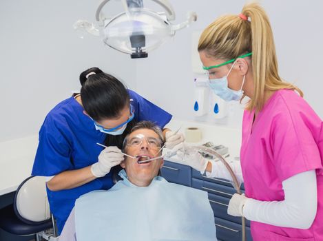 Dentist examining a patient with her dental nurse holding suction hose