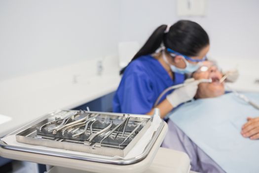 View of tray of dental equipment in front of a dentist with a patient 