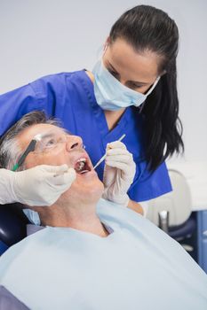 Dentist wearing surgical mask examining patient with tools