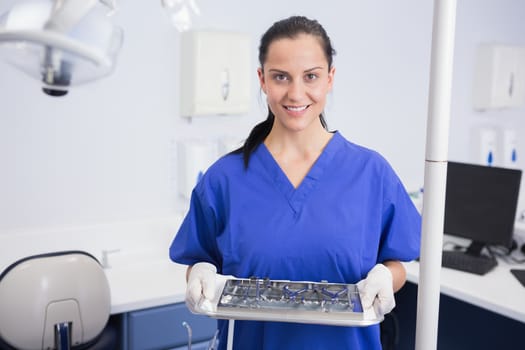 Portrait of a smiling dentist holding tray with equipment in dental clinic