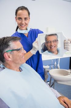 Smiling dentist showing teeth of her patient with a mirror in dental clinic