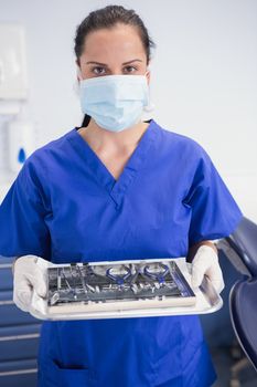 Portrait of a dentist with surgical mask and holding tray in dental clinic