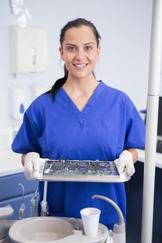 Portrait of a smiling dentist holding tray with equipment in dental clinic