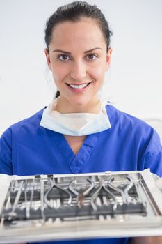 Smiling dentist holding tray with equipment in dental clinic