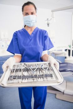 Portrait of a dentist with surgical mask and holding tray in dental clinic