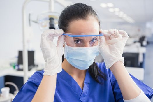 Dentist with surgical mask putting on her safety glasses in dental clinic 