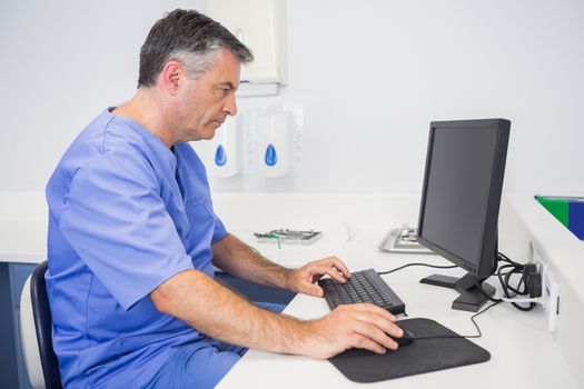 Serious dentist sitting and using computer in dental clinic