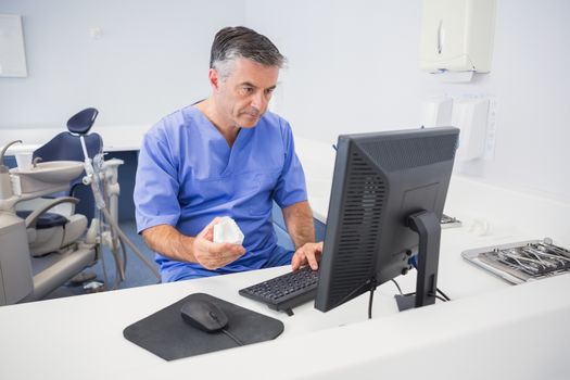 Serious dentist using computer and holding model in dental clinic