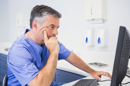 Serious dentist sitting and using computer in dental clinic