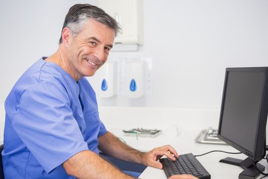 Smiling dentist sitting and using computer in dental clinic