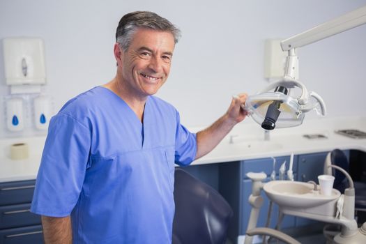 Portrait of a friendly dentist holding light in dental clinic