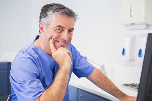 Portrait of a smiling dentist using computer in dental clinic
