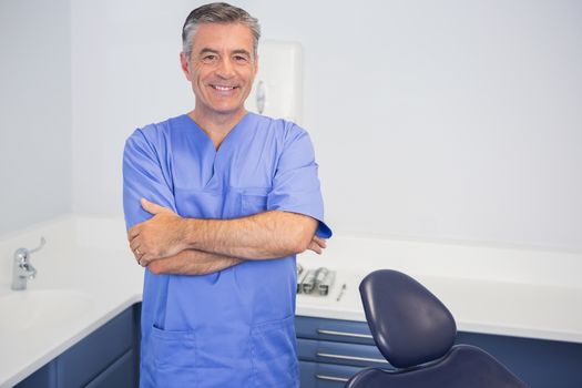 Smiling dentist standing with arms crossed in dental clinic