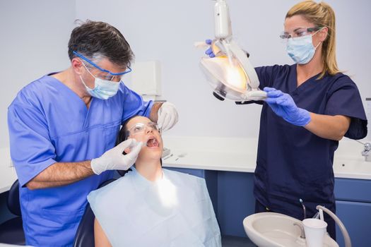 Dentist doing injection to his patient and nurse adjusting the light in dental clinic