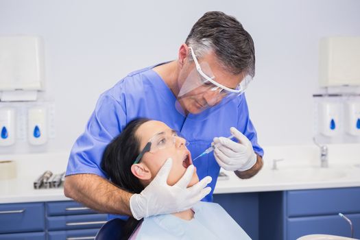 Dentist wearing face shield and doing injection to his patient in dental clinic 