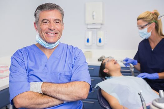 Portrait of a smiling dentist his arms crossed and his nurse with the patient behind him